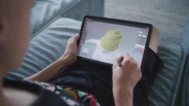 Elinde tablet ve dijital kalemle odaklanmış bir genç odada oturuyor ve 3D modeller çiziyor. Çocuk 3 boyutlu modelleme programı kullanarak yeni oyun karakterleri ve animasyonlar yaratıyor. Oyun tasarımı ve geliştirmesi. Kapat..