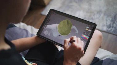 Elinde tablet olan ve dijital stili olan çocuk evde oturup 3 boyutlu modeller yaratıyor. Odaklanmış genç, 3D modelleme programı kullanarak oyun karakteri için kıyafet çiziyor. Geliştirme ve oyun tasarımı konsepti. Kapat..
