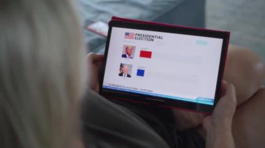 ZAPORIZHYA, UKRAINE - 7 Haziran 2024: Kafkasyalı kadın, ABD başkanlık seçimlerinin son dakika haberlerini tablet bilgisayar kullanarak koltukta yatarken izliyor. Anketler Trump zaferiyle sonuçlandı