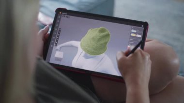 Kadın üç boyutlu tasarım uygulamasında dijital tablet ve stil kullanarak giysiler çizer ve yaratır. Beyaz kadın evdeki kanepede yatarak uzaktan çalışma projesi yapıyor. Yaşam tarzı ve serbest çalışma. Kapat..