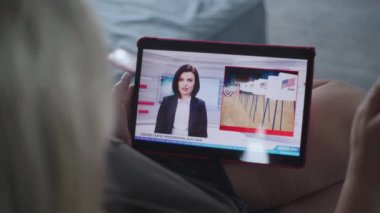 Kanepede yatarken tablet bilgisayar kullanarak ABD başkanlık seçimleriyle ilgili son dakika haberlerini izleyen beyaz kadının görüntülerini kapatıyoruz. Tablet ekranda kadın haber spikeriyle televizyon haberleri yayınlanıyor.