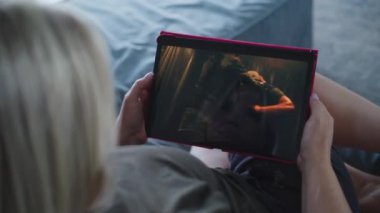 Yetişkin kadın kanepede yatarken tablet bilgisayar kullanarak aksiyon filmi izliyor. Gerilim filmli dijital tablet ekran. Kadın işten sonra evde dinleniyor. Yaşam tarzı konsepti. Kapat..