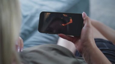 Beyaz kadın koltukta yatarken akıllı telefon kullanarak aksiyon filmi izliyor. Mobil telefon ekranında gerilim filmi gösteriliyor. Beyaz kadın hafta sonları evde dinleniyor. Yaşam tarzı konsepti. Kapat..