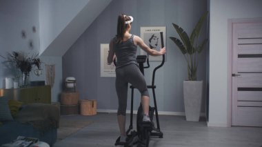 Sanal gerçeklik kulaklığı takan bayan sporcu, yörünge simülatöründe çalışmaya başladı. Ekranda manzara arkaplanı ve VR spor uygulamasının arayüzü görülüyor. Metaverse fütüristik spor salonu. VFX canlandırması.