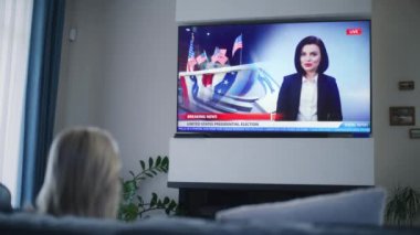 Yetişkin bir kadın, Amerika Birleşik Devletleri seçimleri ile ilgili haber bültenini kanepede oturan büyük TV ekranında izliyor. TV ekranında yayınlanan kadın haber spikeriyle ilgili son dakika haberleri. Arka plan.