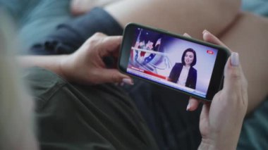 Yetişkin bir kadının, Amerika Birleşik Devletleri 'ndeki seçimlerle ilgili haberleri izlerken evdeki kanepede uzanırken akıllı telefon kullanarak yayınladığı statik görüntüleri kapatın. ABD 'de Seçim Günü.