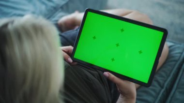 Yeşil ekranlı tablet bilgisayarı tutan ve kanepede uzanan video içeriği izleyen bir kadının arka planı. Yetişkin beyaz kadın hafta sonları evde dinleniyor. Yaşam tarzı konsepti. Krom anahtar. Kapat..