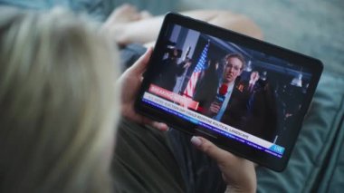 Beyaz kadının ABD Seçim Günü ile ilgili son dakika haberlerini izlerken kanepede otururken tablet bilgisayar kullanmasını kapatın. Tablet ekranında görüntülenen kadın gazetecinin haber kaydı.
