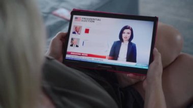 ZAPORIZHYA, UKRAINE - 7 Haziran 2024: Kafkasyalı kadın, tablet bilgisayarla koltukta yatarken ABD seçimlerinin oylama sonuçlarını canlı olarak izliyor. Anketler Trump zaferiyle sonuçlandı