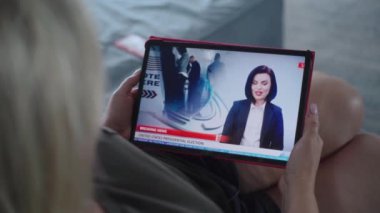 Tablet ekranda kadın haber spikeriyle televizyon haberleri yayınlanıyor. Kanepede yatarken dijital tablet kullanarak ABD başkanlık seçimlerini izleyen beyaz kadın. Kapat..