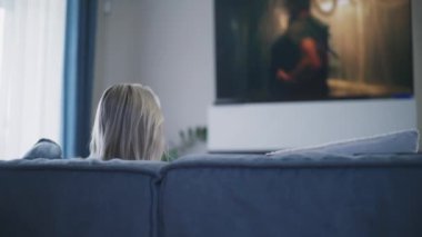 Televizyonda gerilim filmi izleyen bir kadının oturma odasında rahat bir kanepede oturup dinlendiği bir sahne. Büyük TV ekranında aksiyon filmi gösterildi. Ev sineması. Yaşam tarzı kavramı.