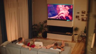 Kafkas ailesi oturma odasındaki kanepede yatar ve akşamları TV 'de aksiyon filmi ya da TV şovu izler. İki çocuklu eşler hafta sonunu evde geçirirler. Ev sineması. Yaşam tarzı konsepti. Yüksek açı.