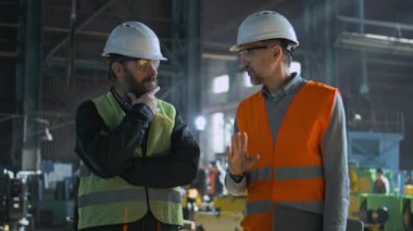 Güvenlik üniformalı iki profesyonel ağır endüstri mühendisi ve sert şapkalar imalat fabrikasında çalışma sürecini tartışıyor. Olgun yönetici, fabrika ya da atölyede çalışan yetişkin işçilerle konuşur. Yavaş çekim.