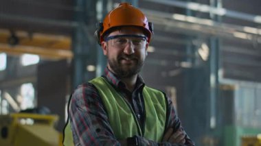 Üretim fabrikasında koruyucu üniforma, kask ve gözlük takan profesyonel ağır endüstri çalışanı. Erkek teknisyen ya da mühendis gülümser ve kameraya bakar. Kurulum tesisi. Portre.