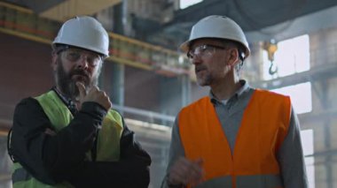 Koruyucu üniformalı ve kasklı iki ağır sanayi teknisyeni fabrikadaki üretim süreci hakkında tartışıyorlar. Olgun müfettiş üretim tesisinde yetişkin çalışanlarla konuşur. Yavaş çekim.