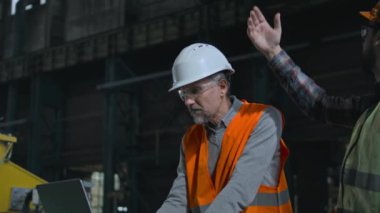 Güvenlik üniformalı profesyonel ağır sanayi mühendisi ve hardhat dizüstü bilgisayar kullanıyor. Erkek işçi endüstriyel makine ekipmanlarını yönetir ve kontrol eder. Fabrika ya da tesis üretimi. Yavaş çekim.