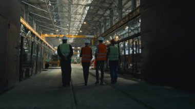 Üniformalı ve miğferli dört ağır endüstri teknisyeni üretim sürecini tartışıyor, fabrikada yürüyor. Erkek ve kadın müfettişler fabrika çalışanlarıyla konuşur. Yavaş çekim.