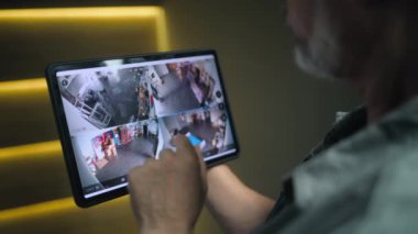 Profesyonel kurucu, şık ofisteki güvenlik kameralarını tablet bilgisayar kullanarak izliyor. Tablet ekranında gösterilen güvenlik kameralarının görüntüsü. İzleme ve izleme. CCTV sistemi ve gizlilik.