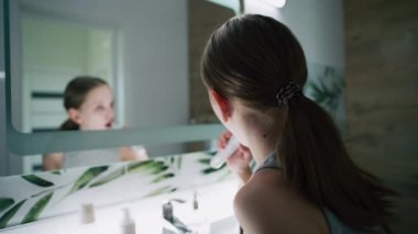 Genç kız banyoda aynaya bakar, dişlerini fırçalar. Güzel genç lavabonun önünde duruyor ve yatmadan önce elektrikli diş fırçası kullanıyor. Akşam banyosu rutini. Yaşam tarzı kavramı. Kapat..