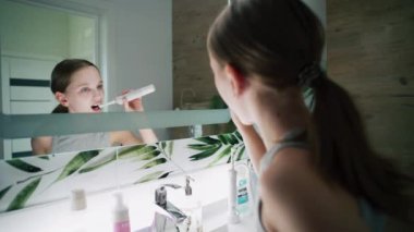 Güzel genç lavabonun önünde duruyor ve yatmadan önce elektrikli diş fırçası kullanıyor. Genç kız banyoda aynaya bakar, dişlerini fırçalar. Akşam banyosu rutini. Yaşam tarzı kavramı. Kapat..