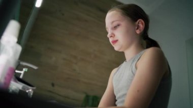 Yumuşak yüzlü güzel bir kız lavabonun yanında durur, yüzünü havluyla siler. Sevimli genç kız banyoya gelir, yüzünü soğuk suyla yıkar ve aynaya bakar. Banyo sabahı rutini.