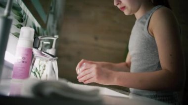 Genç kız lavaboya gelir ve ağzını soğuk suyla çalkalar. Sevimli kız banyoda aynanın önünde duruyor ve yatmadan önce antibakteriyel sıvı kullanarak ağzını çalkaluyor. Banyo akşamı rutini. Kapat..