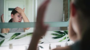 Güzel ergen sabahları lavabonun önünde duruyor ve saçlarını şekillendiriyor. Çekici genç kız banyoda aynaya bakıyor, saç stili yapıyor. Sabah banyosu rutini. Yaşam tarzı kavramı. Kapat..