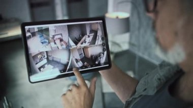 Yetişkin bir erkek teknisyen, ofisteki kapalı devre kameralarını tablet bilgisayar kullanarak izler ve kontrol eder. Tablet ekranda güvenlik kamerası görüntüleri var. İzleme ve izleme. Gözetim sistemi ve mahremiyet.