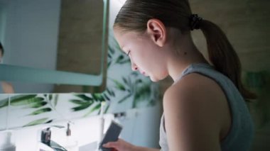 Genç kız banyoda aynaya bakar, dişlerini fırçalar. Güzel genç lavabonun önünde duruyor ve yatmadan önce elektrikli diş fırçası kullanıyor. Akşam banyosu rutini. Yaşam tarzı kavramı. Kapat..