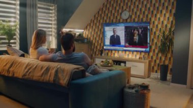 Beyaz çift televizyon ekranında Birleşik Devletler Seçim Günü 'nü izleyip evdeki kanepede oturup çay içiyorlar. Televizyonda yayınlanan son dakika haberiyle siyaset kanalı.
