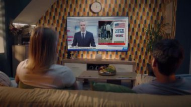Beyaz çift, ABD başkanlık seçimleri ve evdeki kanepede oturan büyük TV ekranında oy kullanma ile ilgili haberleri izliyor. TV ekranında erkek haber spikeriyle flaş haber. Arka plan.