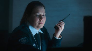 Kadın güvenlik görevlisi ya da polis telsiz kullanıyor, gece vardiyası sırasında iş yerindeki monitörlere bakıyor. Gözetleme, CCTV sistemi ve sosyal güvenlik kavramı.