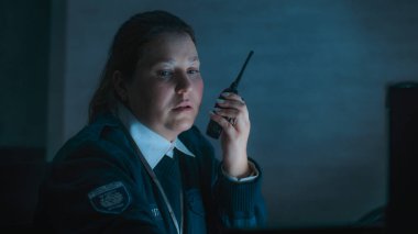 Kadın güvenlik görevlisi ya da polis telsiz kullanıyor, gece vardiyası sırasında iş yerindeki monitörlere bakıyor. Gözetleme, CCTV sistemi ve sosyal güvenlik kavramı.