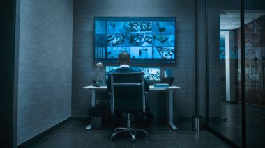 Afrikalı Amerikalı erkek CCTV operatörü ofis güvenlik kameralarını bilgisayar kullanarak kontrol ediyor, modern izleme merkezinde çalışıyor. Güvenlik kamerası görüntülerini gösteren birden fazla monitör ve büyük dijital ekran.
