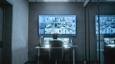 Afrika kökenli Amerikan CCTV operatörü bilgisayardaki güvenlik kameralarıyla ve loş izleme merkezindeki tabletlerle çalışıyor, telsizle konuşuyor. Birden fazla monitörde ve büyük dijital ekranda güvenlik kamerası görüntüleri.