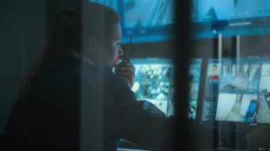 Güvenlik kameralarıyla izleme merkezinde çalışan kadın CCTV operatörünü kapatın, telsizle konuşun. Çoklu monitörler ve güvenlik kamerası görüntülerini gösteren büyük dijital ekran..