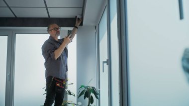 Üniformalı bir erkek, ofis odasındaki güvenlik kamerasını cep telefonunda profesyonel uygulama kullanarak ayarlar. İzleme ve izleme sistemi. Gözetim sistemi, CCTV ve gizlilik kavramı.