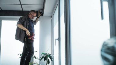 Üniformalı profesyonel erkek teknisyen ofis odasındaki güvenlik kameralarını aletlerle kuruyor ve vidalıyor. İzleme ve izleme sistemi. Gözetim sistemi, CCTV ve gizlilik kavramı.