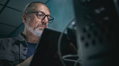 Sunucu rafına kablo yerleştiren yetişkin uzmanları kapatın. Ağ yöneticisi tablet bilgisayar kullanarak sunucu odasında çalışır. Bilgi sistemleri ve ağların işletilmesi. Veri depolama merkezi.