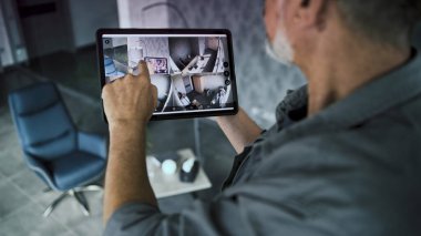Erkek kurucu, kapalı devre kameralarını şık bir ofiste tablet bilgisayar kullanarak izliyor. Tablet ekranda görüntülenen güvenlik kameralarının gerçek zamanlı görüntüsü. İzleme ve izleme. Güvenlik sistemi ve mahremiyet.