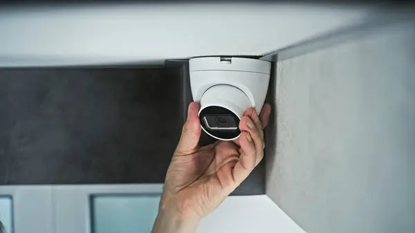 stock image Professional male installer screws CCTV camera to the ceiling in office room using screwdriver tool and adjusts the angle. Monitoring and tracking. Video surveillance, security system, and privacy.