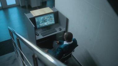 Afrika kökenli Amerikalı erkek güvenlik görevlisi ofisteki iş yerinde oturur, güvenlik kameralarından alınan kamera görüntülerini gösteren bilgisayar monitörüne bakar, telsiz kullanır. Bayan güvenlik görevlisi geçiyor..