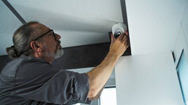 Üniformalı profesyonel bir erkek güvenlik kamerasını ofis odasındaki tavana vidalıyor ve açıyı ayarlıyor. İzleme ve izleme sistemi. Gözetleme sistemi, CCTV ve gizlilik.