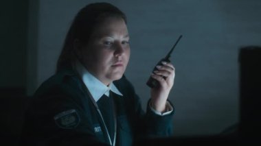 Kadın güvenlik görevlisi ya da polis telsiz kullanıyor, gece vardiyası sırasında iş yerindeki monitörlere bakıyor. Gözetleme, CCTV sistemi ve sosyal güvenlik kavramı.