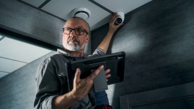 Yetişkin erkek teknisyen, ofis odasına güvenlik kamerası yerleştirmek için profesyonel yazılımlı tablet bilgisayar kullanıyor. Açıyı ayarlıyor. İzleme ve izleme. Güvenlik sistemi, CCTV ve gizlilik.