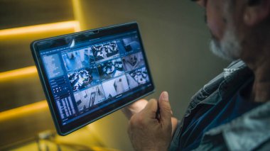 Erkek kurucu, kapalı devre kameralarını şık bir ofiste tablet bilgisayar kullanarak izliyor. Tablet ekranda görüntülenen güvenlik kameralarının gerçek zamanlı görüntüsü. İzleme ve izleme. Güvenlik sistemi ve mahremiyet.
