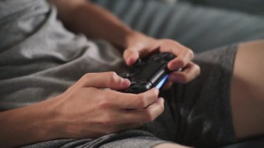 Oturma odasındaki kanepede oturan, kablosuz kumandayı kullanarak internet üzerinden oyun oynayan beyaz çocuğun ellerini kapat. Ergen dinleniyor ve hafta sonunu evde geçiriyor. Yaşam tarzı kavramı.