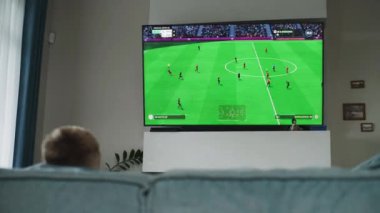 ZAPORIZHYA, UKRAINE - 7 Haziran 2024: Profesyonel genç oyuncu rahat oturma odasında kanepede oturur ve TV ekranında konsol oyunu oynar. Kafkasyalı genç boş vakitlerini harcıyor