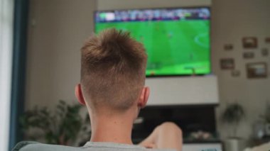 Kafkasyalı bir gencin televizyondaki konsolda kablosuz kumandayı kullanarak online futbol oyunu oynaması, rahat oturma odasındaki kanepede oturması. Gençler hafta sonunu evde geçiriyor. Yaşam tarzı kavramı