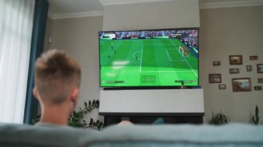 ZAPORIZHYA, UKRAINE - 7 Haziran 2024: Kafkasyalı genç çocuk büyük TV ekranında konsol oynuyor oturma odasında rahat bir oturma odasında kanepede otururken.